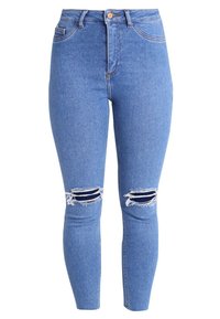 Jeans de mezclilla azul de cintura alta con un corte slim, que presentan desgastes en las rodillas con bordes deshilachados y parches de mezclilla oscura contrastante debajo.