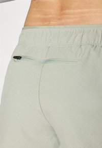 Shorts de sport vert clair avec une surface texturée, dotés d'une poche zippée à l'arrière et d'une ceinture élastique pour un meilleur ajustement.