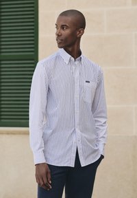 Camicia a righe blu e bianca con taschino sul petto, realizzata in tessuto leggero, con maniche lunghe e collo.