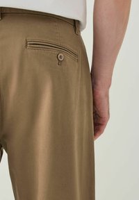 Brown trousers featuring a smooth texture, tailored fit, and a back pocket with a button closure.
