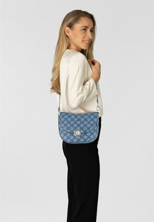 Blaue, gemusterte Umhängetasche aus Textil mit Klappverschluss und einem runden silbernen Metallakzent. Über der Schulter getragen.