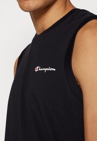 Svart ärmlös t-shirt i bomull med rund hals. Har en röd och vit "Champion"-logotyp på övre vänstra sidan.