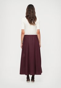Jupe maxi bordeaux avec des plis; associée à un haut ajusté rayé blanc. La tenue a une texture douce et une taille élastique.