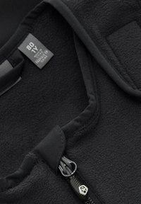 Svart fleeceväst med en slät dragkedja och tygmärke, som har ett mjukt, strukturerat inre och en ren, minimalistisk design.