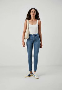 Tynne blå jeans laget av denim, høyt liv med glidelås. Kombinert med en hvit tanktop og hvite sneakers med blå striper.