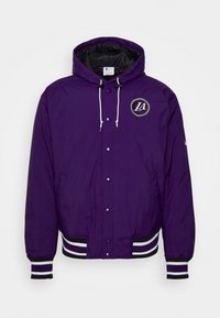 Lila, isolerad jacka med huva och svart foder. Har en framlogo och randiga ribbade muddarna och nederkant. Tryckknapps-stängning.