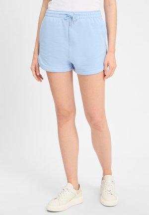 Shorts en coton bleu clair avec une taille élastique, des détails à cordon de serrage et un ourlet arrondi. Portés avec des baskets blanc cassé.