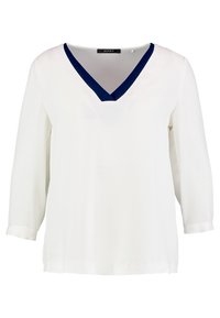 Blouse blanche à manches longues avec un col en V de couleur bleu marine et une coupe décontractée.