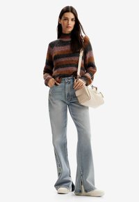 Maglione lavorato a maglia multicolore con collo alto, abbinato a jeans chiari a zampa d'elefante con spacchi all'orlo. Include una borsa a spalla beige.