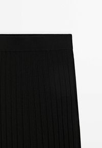 Ceinture et partie supérieure d'une jupe en tricot côtelé noir, montrant des lignes texturées verticales sur fond blanc.