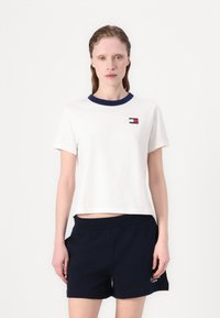 Hvid cropped t-shirt med en marineblå krave, der har et lille logo-patch. Parret med marineblå shorts, der udviser en glat tekstur og et afslappet design.