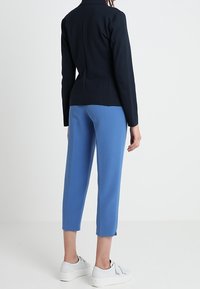 Mörkblå figursydd blazer med enkel krage, i kombination med högmidjade ljusblå byxor och vita sneakers. Släta texturer och rena linjer.