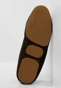 Semelle d'une chaussure marron foncé avec trois patins en caoutchouc beige lisse sur le talon, la voûte plantaire et la boule de pied, photographiée sur un fond blanc d'angle.
