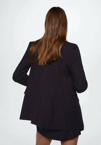 Tmavě pruhovaný blazer s přiléhavým střihem, mírně delší zadní částí, klopovými límci a dvěma předními kapsami. Hladká tkanina s klasickým designem.