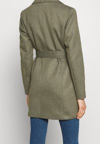 Olivově zelený kabát z vlněné směsi s páskem v pase, strukturovanými rameny a hladkou texturou, s designem do poloviny stehna.