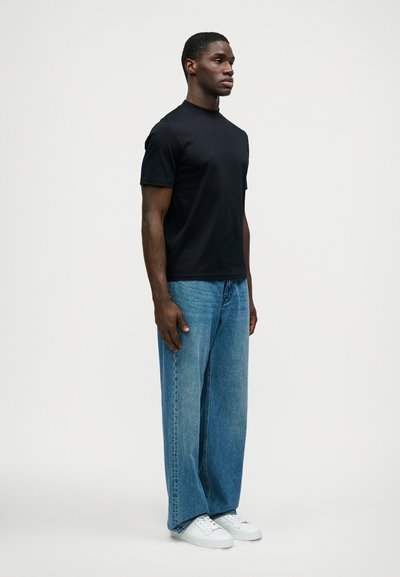 Μαύρο κοντομάνικο μπλουζάκι, άνετη εφαρμογή, συνδυασμένο με ανοιχτό μπλε παντελόνι φάρδυ. Λευκά αθλητικά παπούτσια, απλός σχεδιασμός, μινιμαλιστικό στυλ.