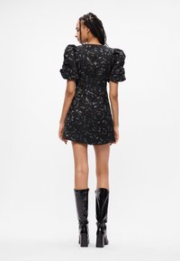 Crna haljina s cvjetnim uzorkom, nabranim rukavima i prilijepim siluetom. Nosila se uz visoke sjajne crne čizme do koljena.