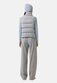 Grå polstret vest med høj krave, båret over en lyseblå langærmet top. Grå bukser og en ribbet lyseblå hue fuldender outfittet.