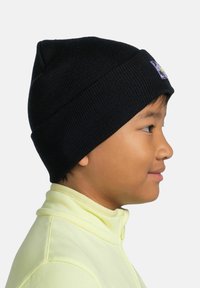 Black knit beanie with a ribbed texture and a small colorful patch on the front. Worn by a child with a light yellow collar.