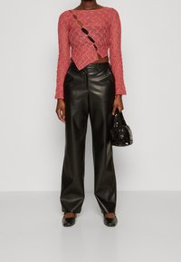 Persona che indossa un top a maniche lunghe in pizzo rosa strappato, pantaloni larghi in pelle nera, tacchi neri e tiene in mano una piccola borsa nera di paillettes.