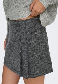 Jupe texturée grise avec un motif subtil, coupe ajustée, dotée de plis et d'un ourlet anglé. Se marie bien avec un haut en maille gris clair.