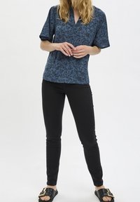 Camicia a fiori blu navy con maniche corte e scollatura a V, abbinata a jeans skinny neri e sandali neri con fibbia dorata.