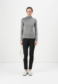 Grå langærmet turtleneck-top parret med sorte leggings, hvide slip-on sko og en lysefarvet crossbody-taske med teksturdetaljer.