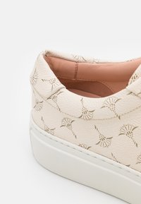 Talons de baskets couleur crème avec un motif floral subtil, col rembourré, intérieur beige clair et semelle blanche épaisse.