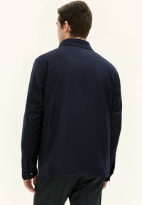 Camicia a maniche lunghe blu navy con colletto, caratterizzata da una texture uniforme e polsini con bottoni, vista di spalle.