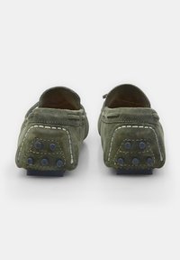 Grüne Wildleder-Slipper mit abgerundeter Form, kontrastierenden weißen Nähten und einer strukturierten Gummisohle mit blauen Traktionspunkten.