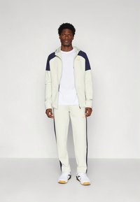 Svetlosivé športové oblečenie pozostávajúce z bundy na zips s námorníckymi detailmi a bielym tričkom, doplnené o zladené tepláky a biele tenisky.