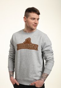Sweatshirt grigio con un logo "BROWN" marrone e una grafica di un orso. Maniche lunghe, scollo rotondo e polsini e orlo a coste.