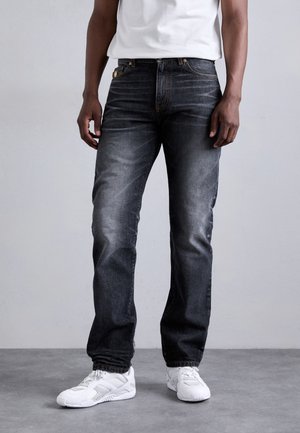 Dark grey denim jeans with a straight cut, faded wash, and orange stitching, paired with white sneakers. Features front pockets and a button fly.