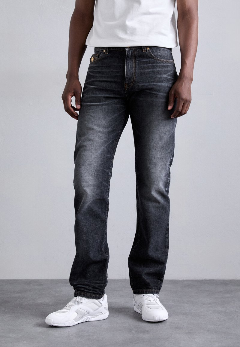 Jeans din denim gri închis cu un croi drept, spălare ușor decolorată și cusături portocalii, asortați cu sneakerși albi. Au buzunare frontale și închidere cu nasture.