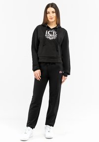 Black cropped hoodie with a silver logo, paired with black joggers featuring a pink logo, complemented by white sneakers. Smooth fabric texture.