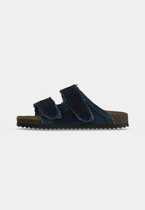 Sandale slide en denim bleu foncé avec deux sangles réglables, semelle intérieure en liège et semelle extérieure noire en zigzag, vue de côté sur fond blanc.