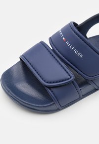 Granatowe klapki z dwiema regulowanymi rzepami, gładkiego materiału syntetycznego i teksturowanym wnętrzem dla komfortu.