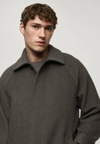Dark gray wool coat with large collar, raglan sleeves, and minimal seam detailing. Soft texture, button closure, and a relaxed fit.