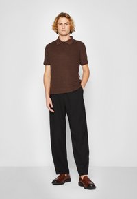 Polo shirt de color marrón con cuello marrón, combinado con pantalones negros holgados y mocasines de cuero marrón. Diseño simple y minimalista.