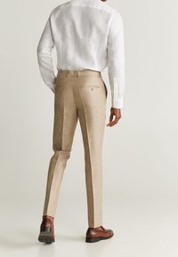 Beżowe lniane spodnie o dopasowanym kroju, z dwoma tylnymi kieszeniami i subtelnym połyskiem, w zestawie z brązowymi skórzanymi butami.