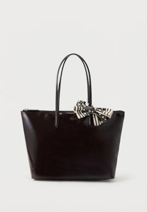 Sac fourre-tout en cuir verni noir avec deux sangles d'épaule et un nœud à motifs noir et blanc attaché près de la poignée.