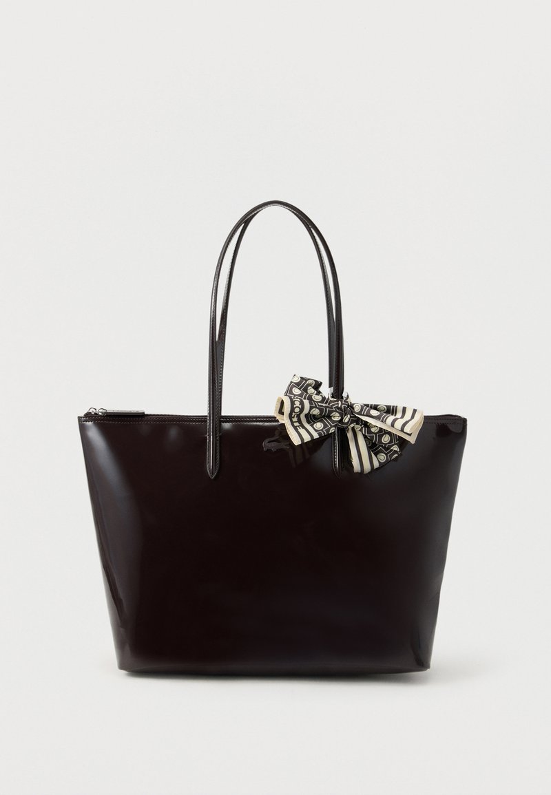 Sac fourre-tout en cuir verni noir avec deux sangles d'épaule et un nœud à motifs noir et blanc attaché près de la poignée.