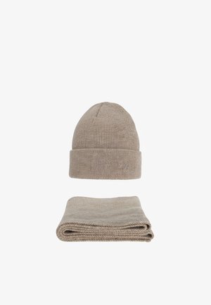 Bonnet d'hiver en maille beige avec petit logo brodé au-dessus d'une écharpe assortie beige en maille pliée, sur fond blanc.