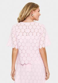 Pink lace top featuring scalloped sleeves and a floral pattern. The back has a slightly loose fit and a nipped waist for added shape.
