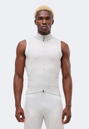 Jeune homme aux cheveux blonds courts portant un haut de sport ajusté sans manches gris clair zippé et un short de cyclisme assorti.