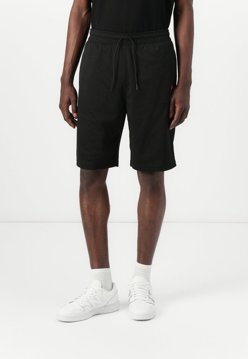 Black mesh athletic shorts with an elastic waistband and drawstring. Features a knee-length cut and subtle logo detail. Paired with white sneakers.