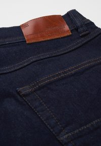 Dunkelblaue Denim-Jeans mit einer gesteppten Gesäßtasche und einem braunen Lederetikett mit der Aufschrift "bugatti Authentic Denim EST 1978" am Bund.