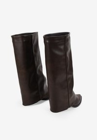 Un par de botas de cuero marrón oscuro hasta la mitad de la pantorrilla con punta cuadrada y discretos detalles de costura sobre un fondo blanco.