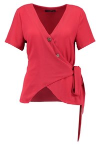 Haut portefeuille rouge à manches courtes, col en V, deux boutons décoratifs et un détail de nouage sur le côté, en tissu texturé.