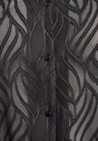 Čierna priehľadná tkanina s vystúpenými vyšívanými vzormi listov a tromi čiernymi gombíkmi v strede.